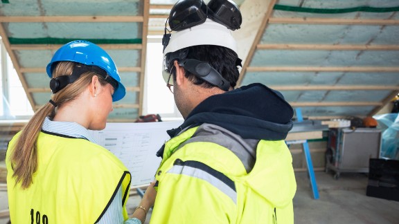 To personer med hjelme og veste planlægger bygning